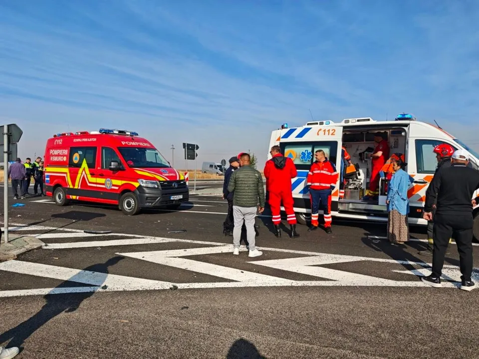 O echipă de intervenție stă lângă două vehicule de urgență, una roșie și una albastră, pe o suprafață asfaltată cu marcaje de trecere de pietoni.