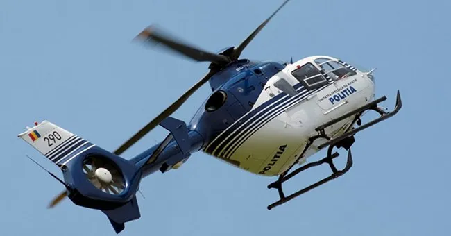 Un elicopter albastru și alb cu inscripția POLITIA zboară pe un cer senin.
