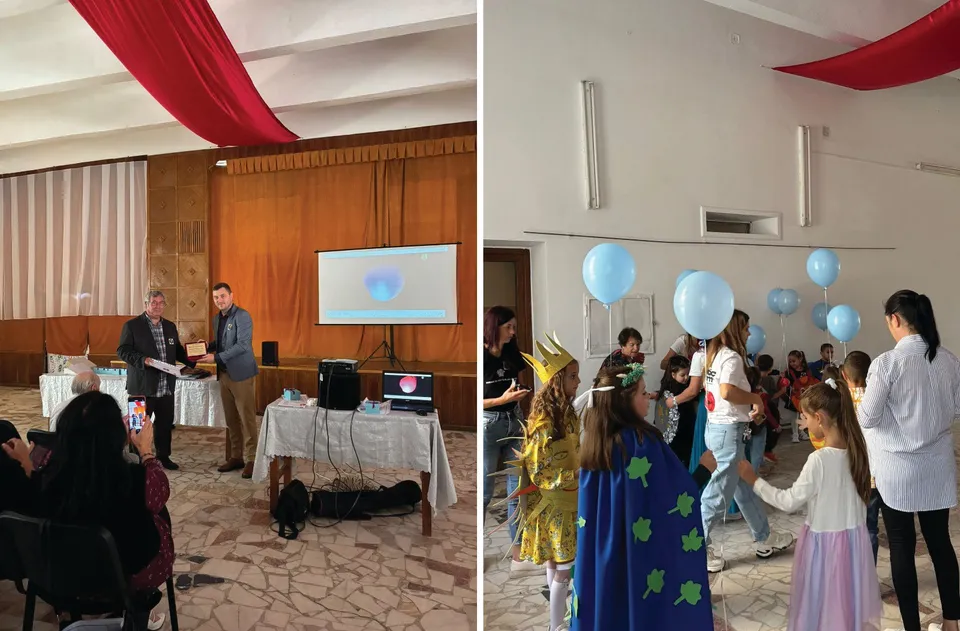 Un grup de copii în costume colorate stă într-o încăpere cu decoruri roșii, în timp ce unii adulți observă scena.