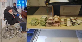Un bărbat cu barbă și căciulă stă într-un scaun cu rotile, lângă mese pe care sunt așezate mai multe teancuri de bancnote.