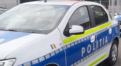 Un autovehicul alb cu marcaje albastre și galbene pe care scrie textul POLITIA este parcat pe o stradă.