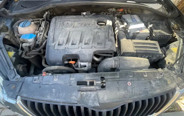 O vedere de sus asupra unui compartiment motor de mașină care conține o baterie, un rezervor de lichid și diverse componente mecanice.