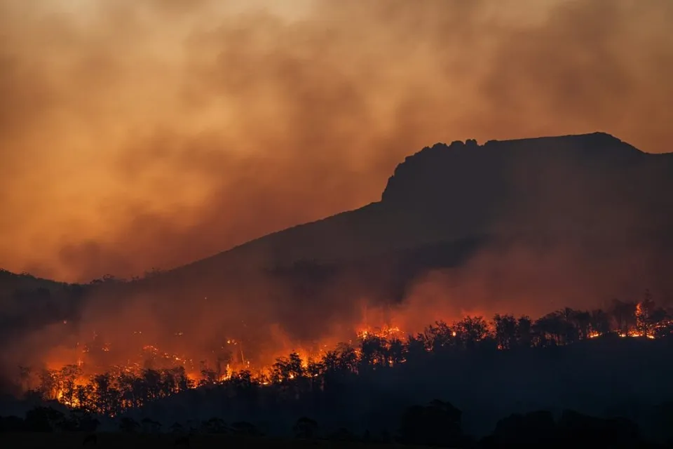 Focul arde pe o creastă de deal sub un cer acoperit de fum dens și gălbui.