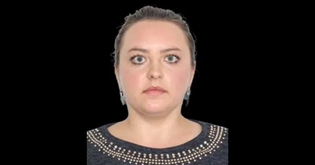 O femeie cu părul strâns în spate și cercei argintii poartă un tricou gri cu detalii metalice la guler pe un fundal negru.