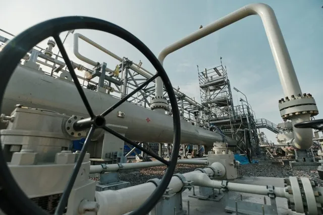 Unelte metalice și conducte gri sunt conectate într-o stație industrială sub un cer deschis.