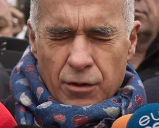 Un bărbat cu părul scurt și gri poartă o eșarfă albastră cu modele colorate, având ochii închiși și gura ușor deschisă.