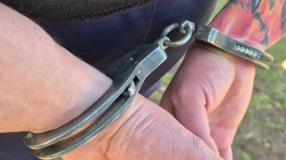 Două mâini cu pielea deschisă la culoare sunt legate cu o pereche de cătușe metalice.