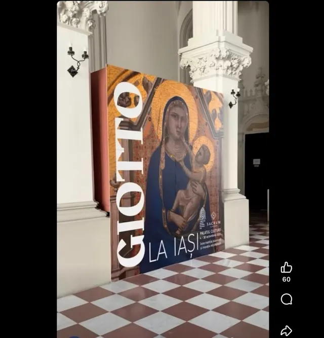Un panou vertical mare afișează o pictură cu o femeie purtând un copil, situat într-un coridor cu podea în model de șah și coloane albe.