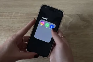 Două mâini țin un smartphone pe o suprafață de lemn, afișând pe ecran un grup de trei pictograme de aplicații sociale sub textul social.