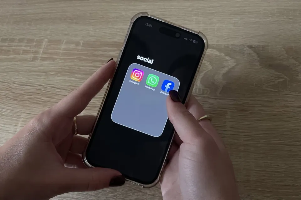 Două mâini țin un smartphone pe o suprafață de lemn, afișând pe ecran un grup de trei pictograme de aplicații sociale sub textul social.