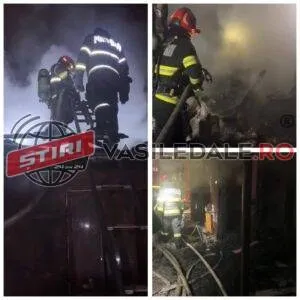 Pompieri în echipament de protecție și casci lucrează noaptea printre fum și resturi de structuri de lemn.