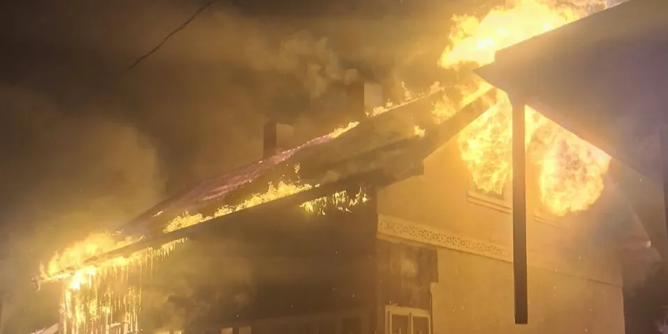 Flăcări mari și fum dens emană de pe acoperișul unei clădiri într-un cadru nocturn.