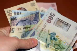 O mână ține mai multe bancnote de lei românești de valori de cincizeci și cinci sute.