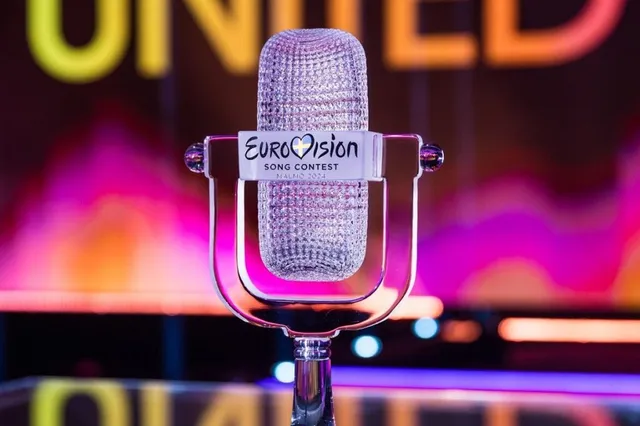 Un microfon argintiu cu logo-ul Eurovision Song Contest este poziționat în centrul unei imagini cu fundal colorat și difuz.
