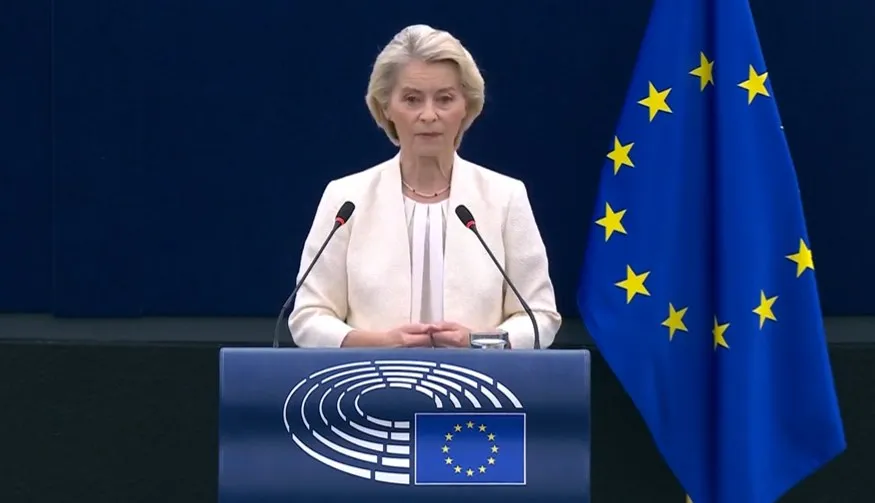 Ursula von der Leyen vorbește la un pupitru, cu steagul Uniunii Europene în dreapta sa, într-o sală de conferințe.