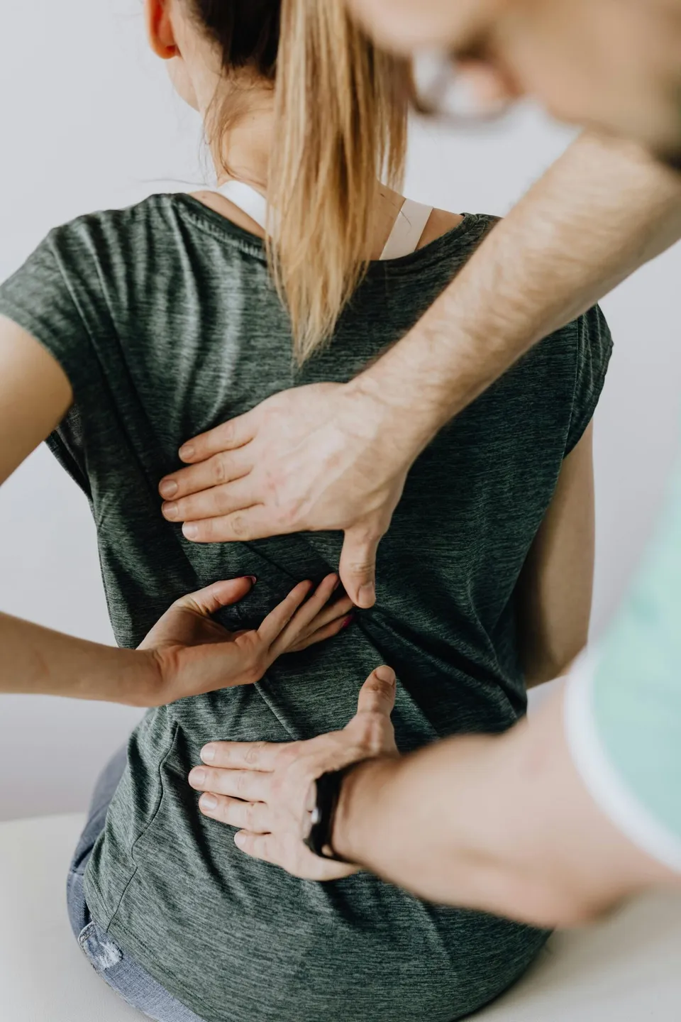 Mai mulți oameni ating spatele unei persoane care poartă un tricou gri și pantaloni scurți de culoare deschisă.