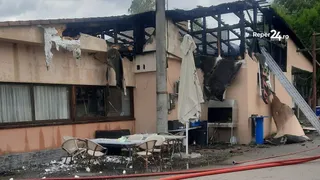 O clădire cu fațada deteriorată și acoperișul carbonizat prezintă resturi de materiale și mobilier de grădină pe un teren de pietriș.