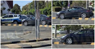 Un autoturism negru este poziționat pe bordura unei insule de separare, lângă un vehicul de poliție albastru și alb.