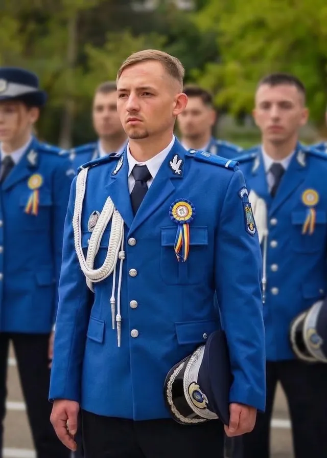 Cinci bărbați în uniforme albastre de serviciu stau în picioare în linie, cel din față purtând o aiguillette albă și un medalion colorat.