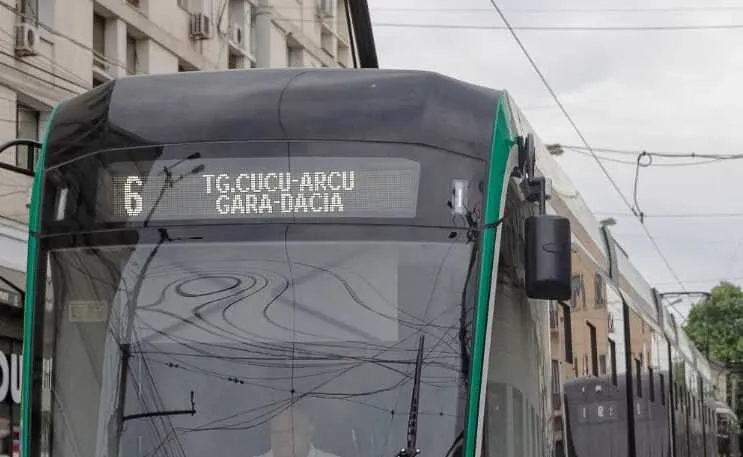 Un tramvai modern cu numărul 6 afișat pe panoul digital circulă pe o stradă cu clădiri în fundal.