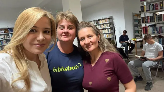 Trei femei poză în prim-plan, una purtând un tricou alb, una un tricou albastru cu inscripție galbenă și una un tricou purpuriu.