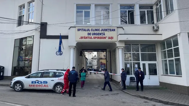 O mașină albă cu inscripția BGS MEDICAL este parcată în fața unei clădiri albe cu ferestre mari, lângă câțiva oameni pe trotuar.