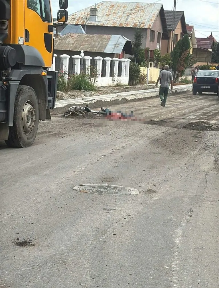 O autoutilitară galbenă este parcată pe marginea unui drum asfaltat lângă un om întins pe carosabil și un bărbat care merge pe trotuar.