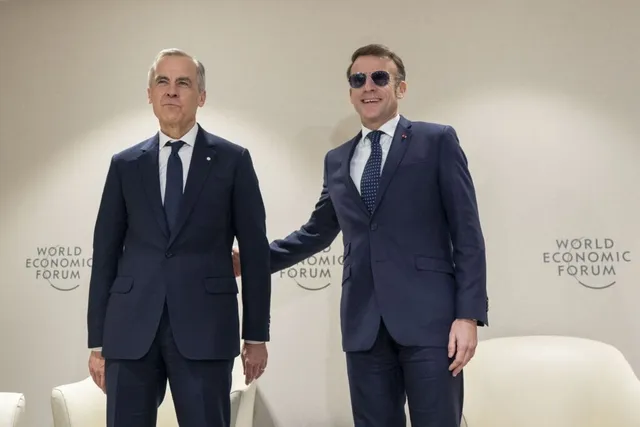 Doi bărbați în costume închise de culoare stau în picioare în fața unui perete alb cu logoul World Economic Forum.