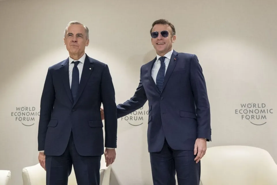 Doi bărbați în costume închise de culoare stau în picioare în fața unui perete alb cu logoul World Economic Forum.