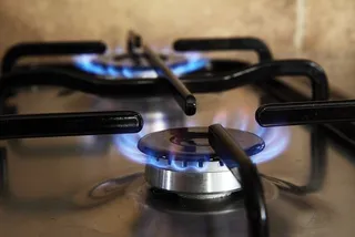 A close-up view of a gas stove with two burners lit, showing bright blue flames and black metal grates.
