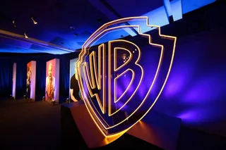 Un logo mare, iluminat cu neon galben și albastru, este poziționat într-o încăpere întunecată cu lumini albastre și panouri verticale în fundal.