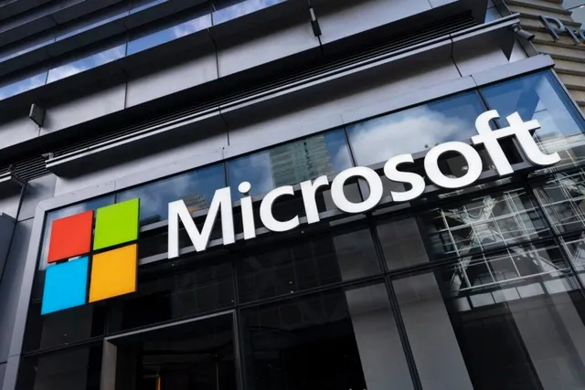 Imaginea arată o clădire modernă cu logo-ul Microsoft, alcătuit din patru pătrate colorate și numele companiei pe un panou de sticlă.