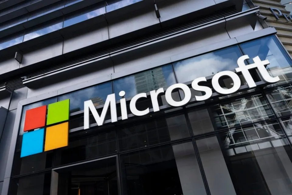 Imaginea arată o clădire modernă cu logo-ul Microsoft, alcătuit din patru pătrate colorate și numele companiei pe un panou de sticlă.