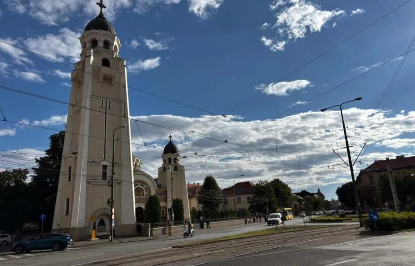 O clădire înaltă cu turn și cupolă neagră se ridică lângă o stradă cu linii electrice suspendate și câteva vehicule circulând.