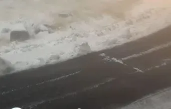 O porțiune de drum asfaltat este parțial acoperită de zăpadă, alături de un gard de protecție îngropat sub un strat gros de zăpadă albă.