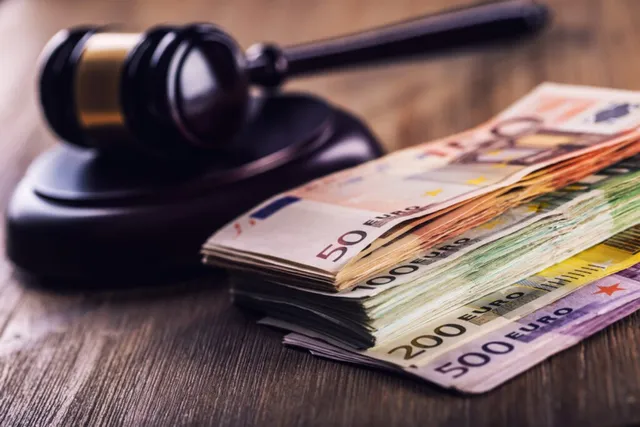 Un ciocan de judecător din lemn stă lângă un teanc de bancnote euro pe o suprafață de lemn.