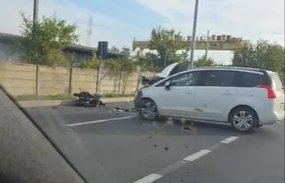 Un autoturism alb este oprit pe carosabil lângă un vehicul de două roți răsturnat pe asfaltul de lângă un gard.