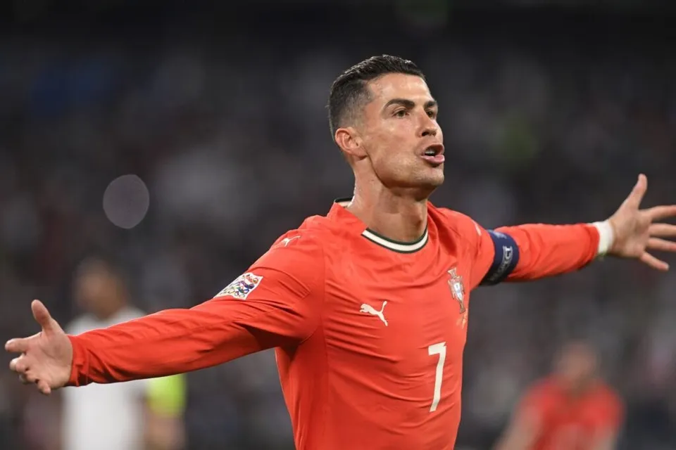 Un bărbat cu tricou portocaliu marcat cu numărul șapte stă cu brațele întinse lateral pe un teren de fotbal.