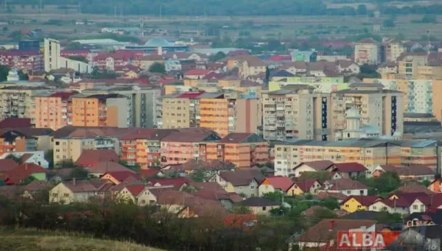 O vedere panoramică asupra unui oraș cu numeroase clădiri rezidențiale de înălțime medie și case cu acoperișuri înclinat sub un cer înnorat.