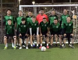 O echipă de minifotbal masculin, în uniformă verde și neagră, cu un portar în roșu, este pozată grupat în fața unei porți de fotbal pe un teren sintetic.