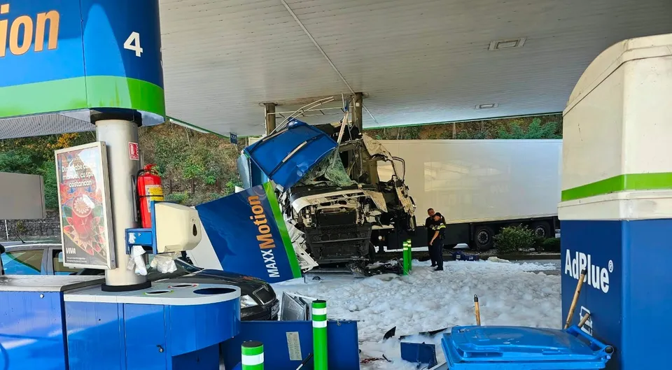 Un autocamion alb cu remorcă este oprit sub acoperișul unei benzinării, lângă o coloană de pompare și pe un sol acoperit de spumă albă.