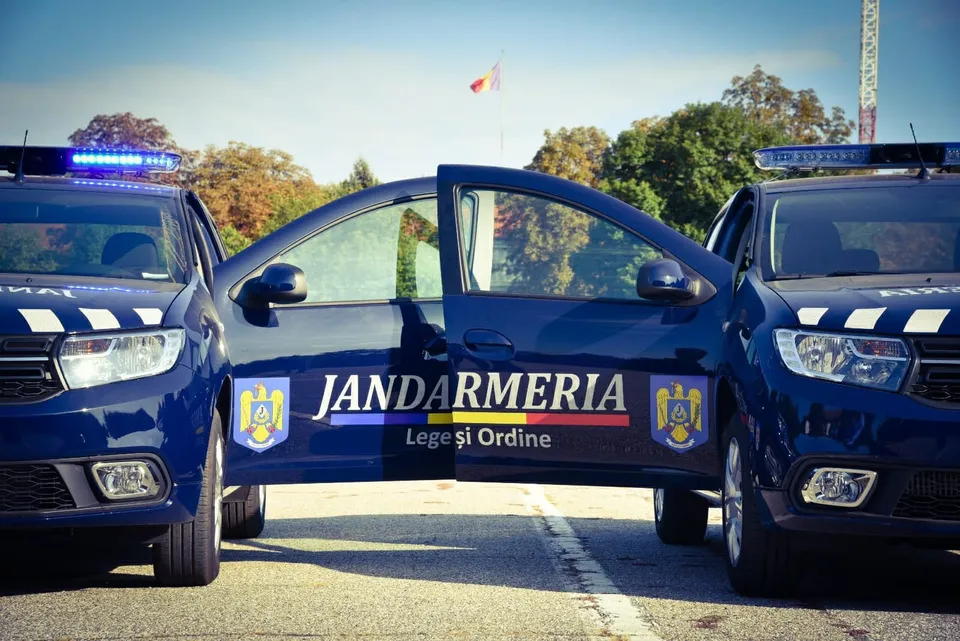 Două mașini de poliție albastre cu portbagajul deschis sunt parcate pe o stradă, având portiera centrală deschisă.