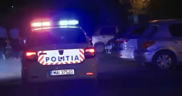 Un autoturism de poliție cu girofaruri aprinse și inscripția POLITIA este parcat pe un drum lângă alte vehicule în timpul nopții.
