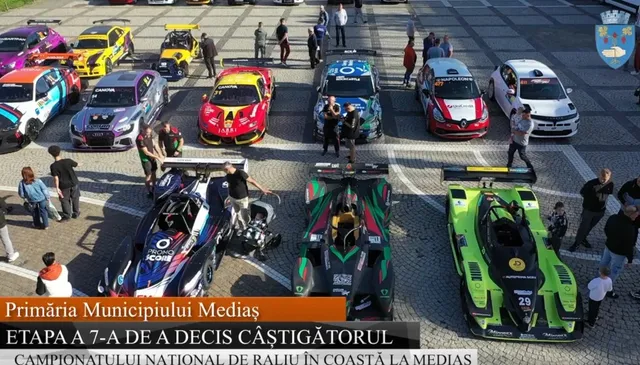 Mai mulți piloți și spectatori stau lângă diverse mașini de curse colorate parcate pe o suprafață asfaltată sub lumina soarelui.
