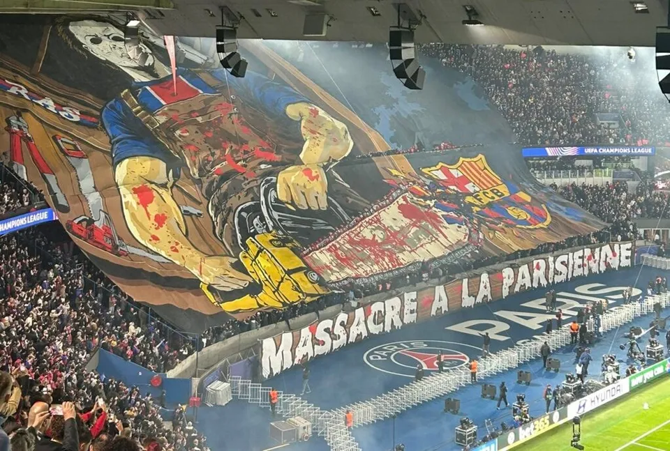 Un banner mare cu o ilustrație de groază și textul MASSARE A LA PARISIENNE este întins deasupra tribunelor unui stadion de fotbal.