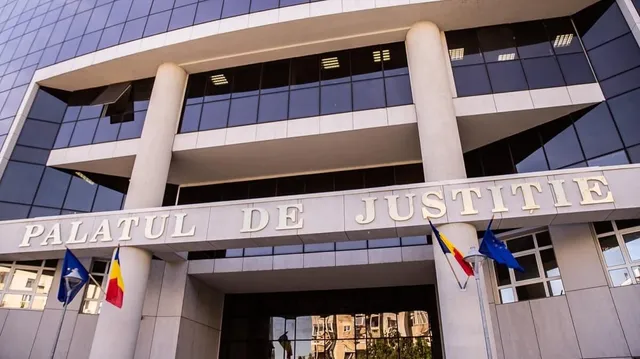O clădire modernă cu ferestre mari și coloane albe prezintă inscripția PALATUL DE JUSTITIE sub care sunt afișate câteva steaguri.