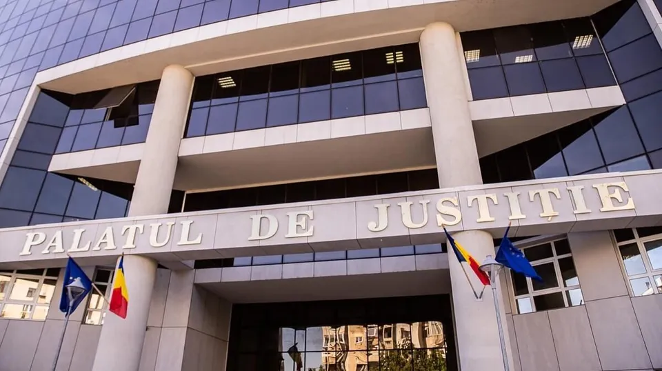 O clădire modernă cu ferestre mari și coloane albe prezintă inscripția PALATUL DE JUSTITIE sub care sunt afișate câteva steaguri.