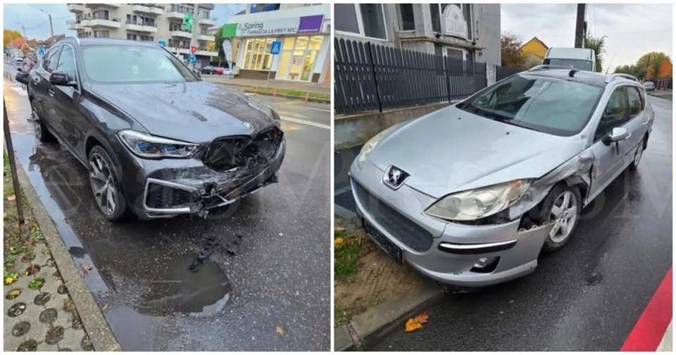 Două mașini avariate, una neagră și una gri, sunt parcate pe un drum asfaltat lângă un trotuar.