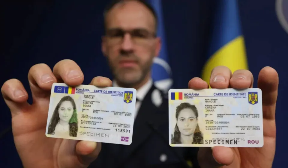 Un bărbat în uniformă ține în prim-plan două documente specimen cu fotografii, embleme și text, în fața unor steaguri.