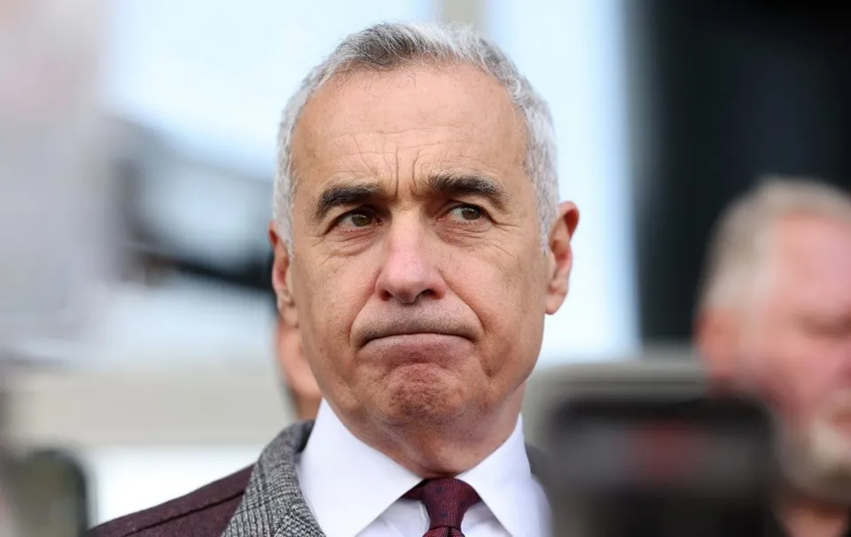 Un bărbat cu părul scurt și cărunt, purtând o cămașă albă, o cravată purpurie și un sacou gri, privește spre lateral.